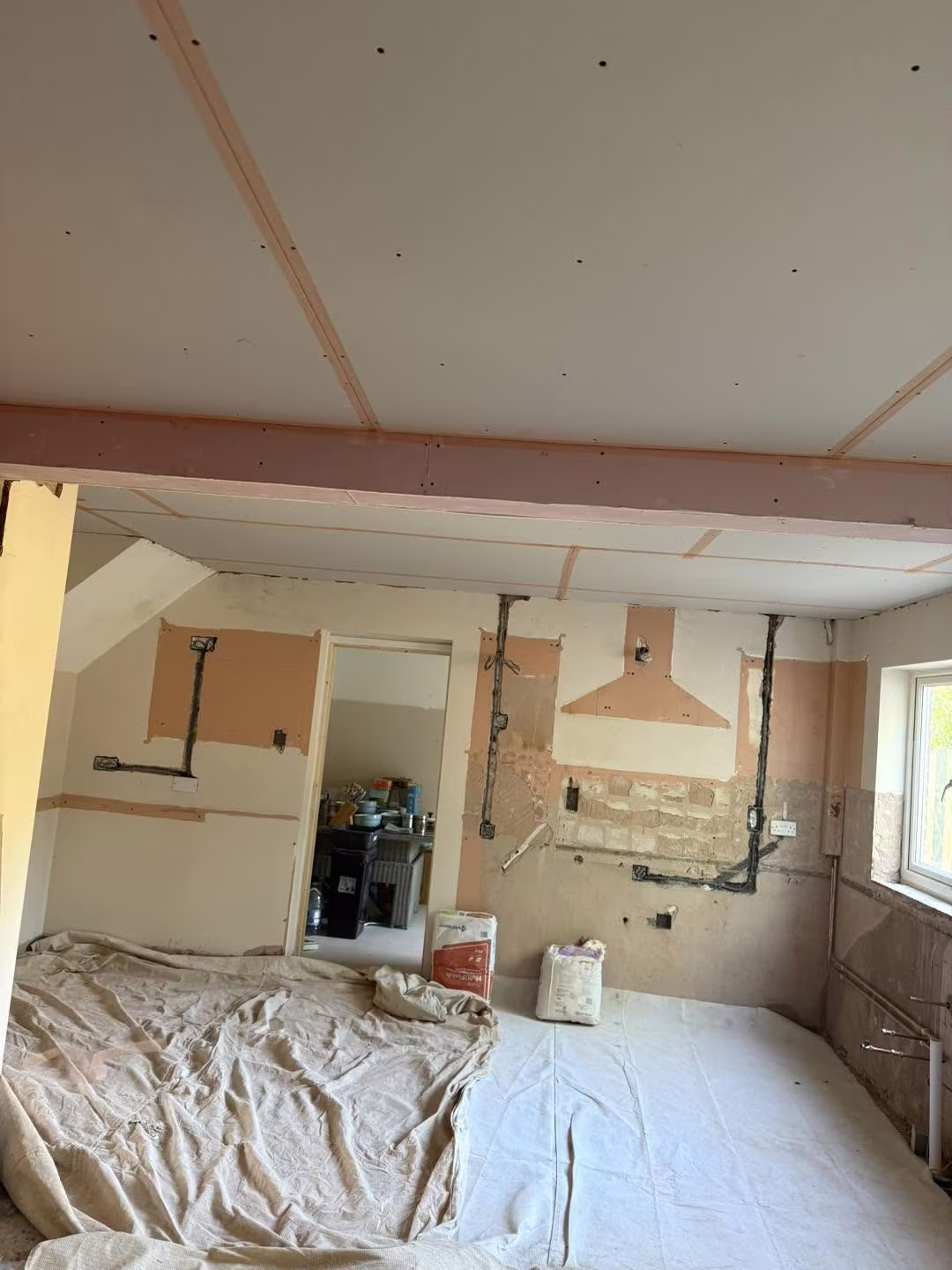 A kitchen ceiling newly plasterboarded and taped either side of a new beam, floor sheeted
